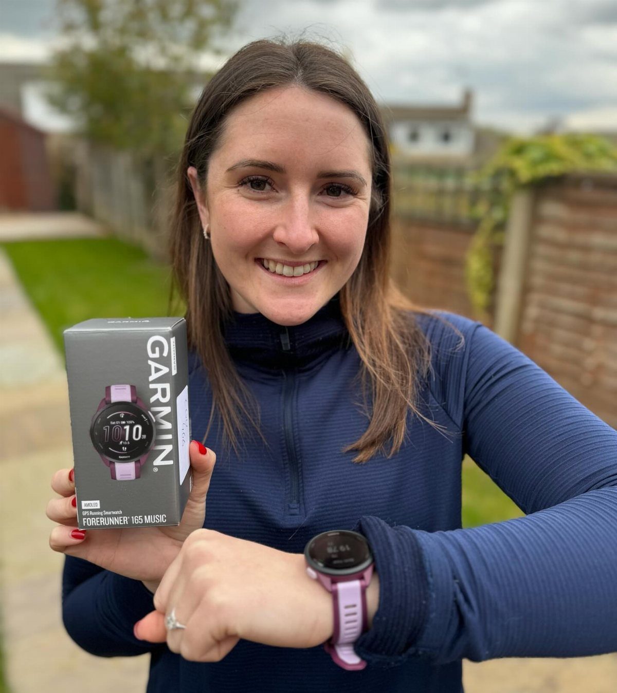 Woman smiling while wearing a purple Garmin watch and holding its product box.