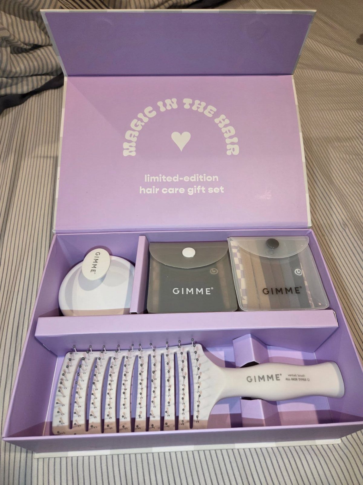 Purple hair care gift set containing a white brush and accessory pouches.