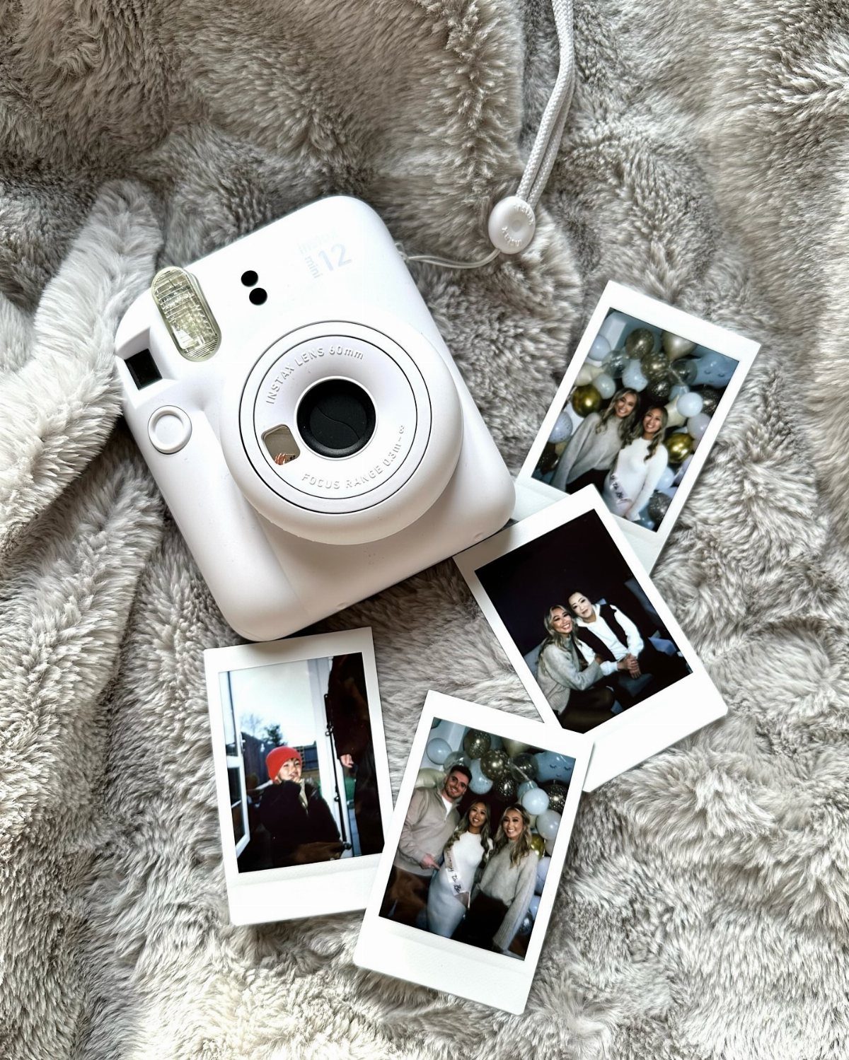 White instant camera and printed polaroid photos on a grey fluffy blanket