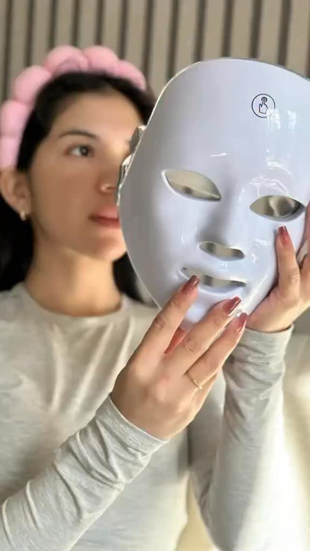 Woman holding a white LED light therapy face mask for skincare treatment.