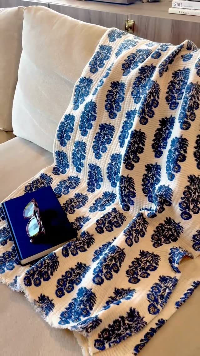 Blue and white floral throw blanket draped over a white sofa with sunglasses.