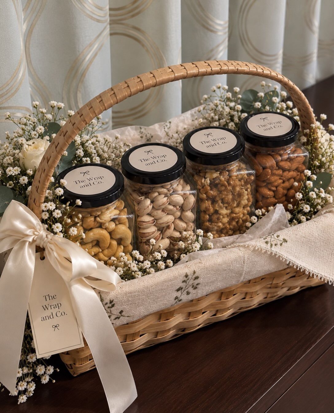 Woven gift basket with four jars of nuts, white flowers, and a cream ribbon.