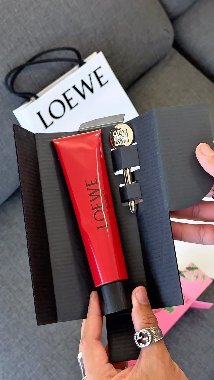 Red Loewe hand cream tube and gold bottle in a black gift box.