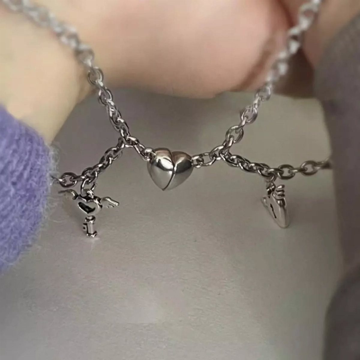 Two silver chains joined by a split heart pendant and small charms.