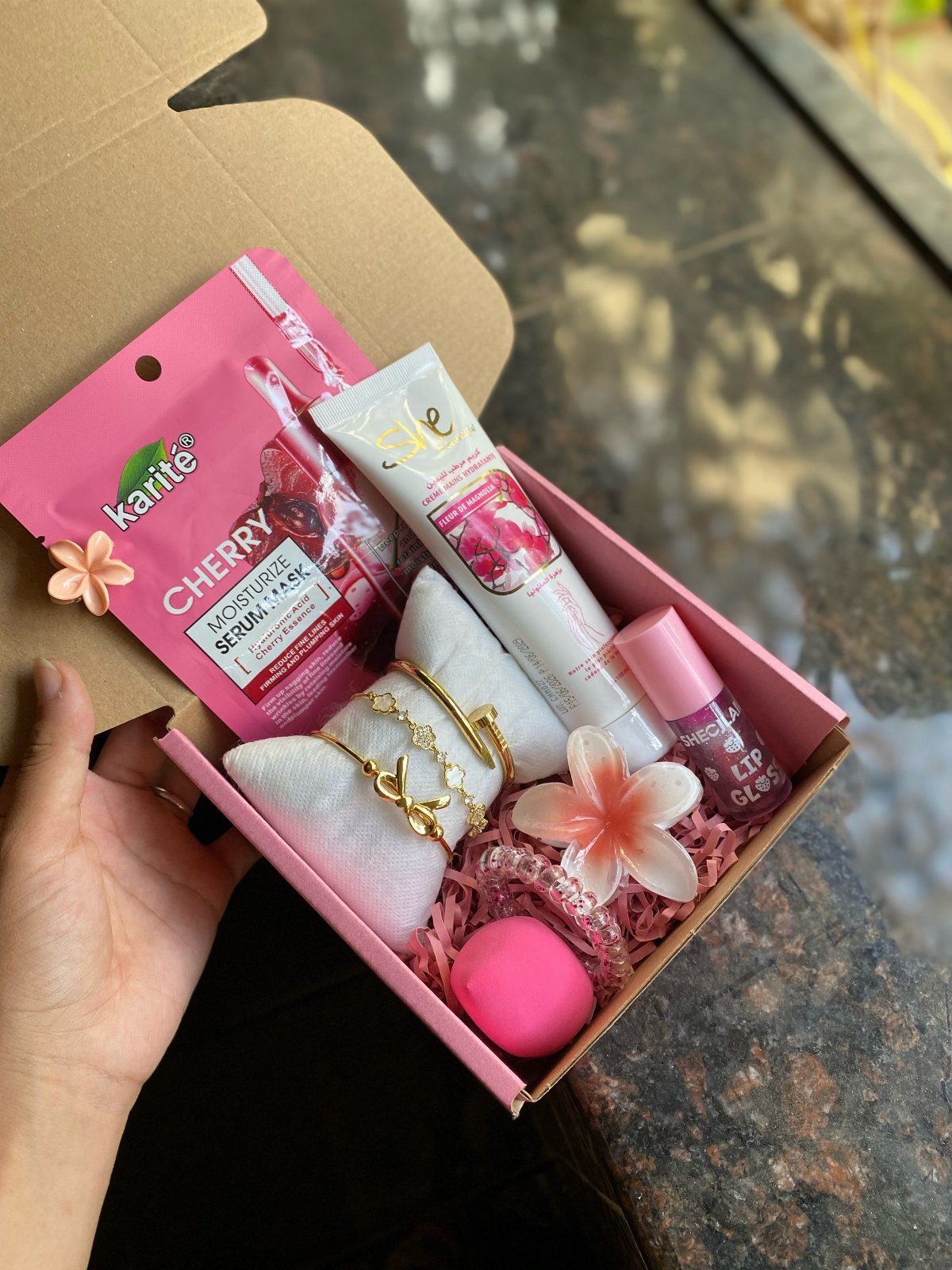 Pink gift box filled with skincare, gold bracelets, and a pink bath bomb.