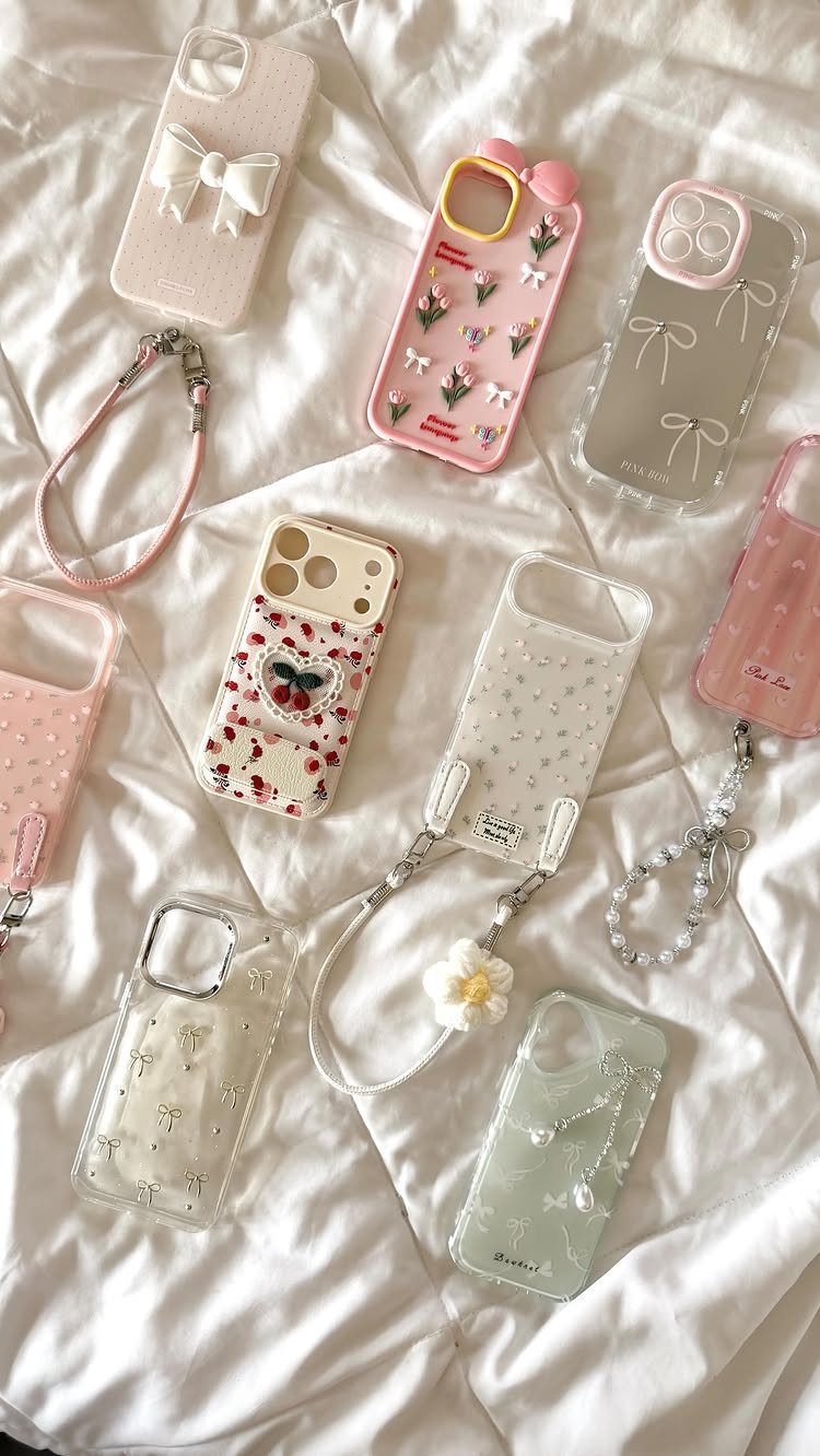 Various decorative feminine phone cases with bows and flowers on white fabric.