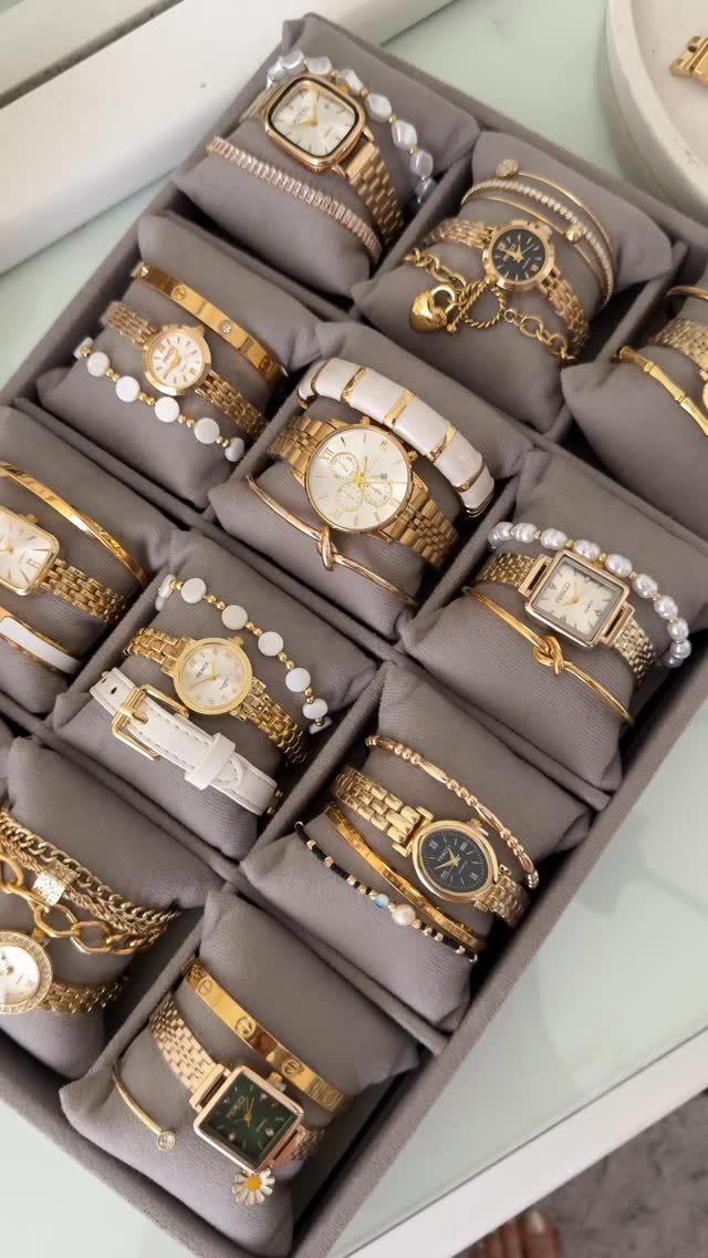 Gold wristwatches and matching bracelets displayed in a grey velvet jewelry organizer box.