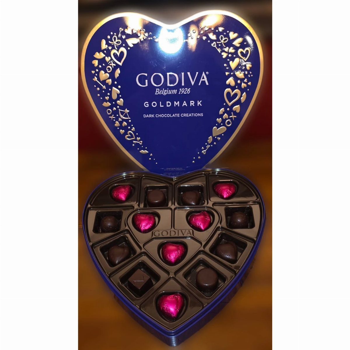 Heart-shaped blue Godiva chocolate box filled with dark and pink heart chocolates.