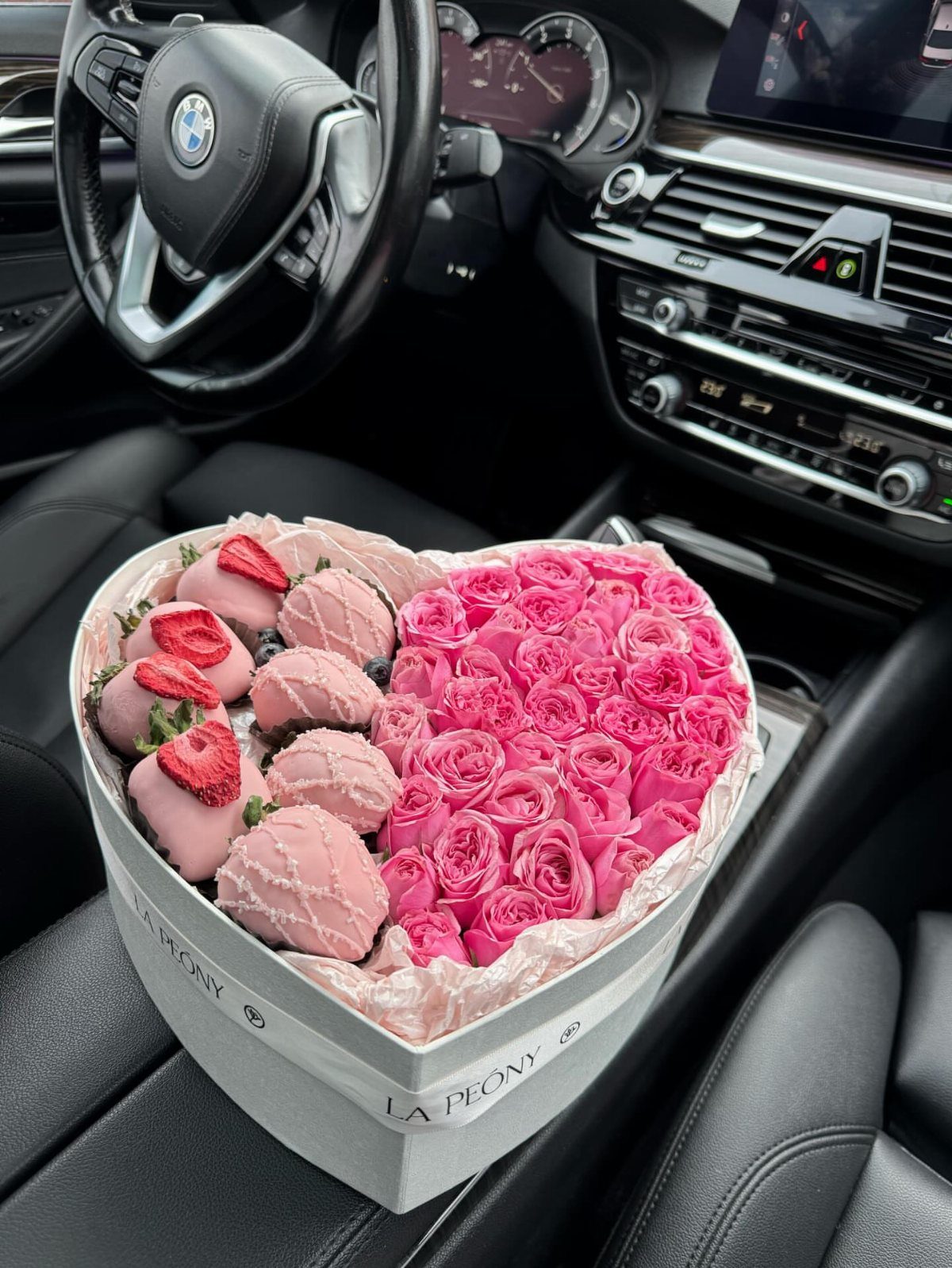 Heart-shaped gift box with pink chocolate-covered strawberries and pink roses in a car