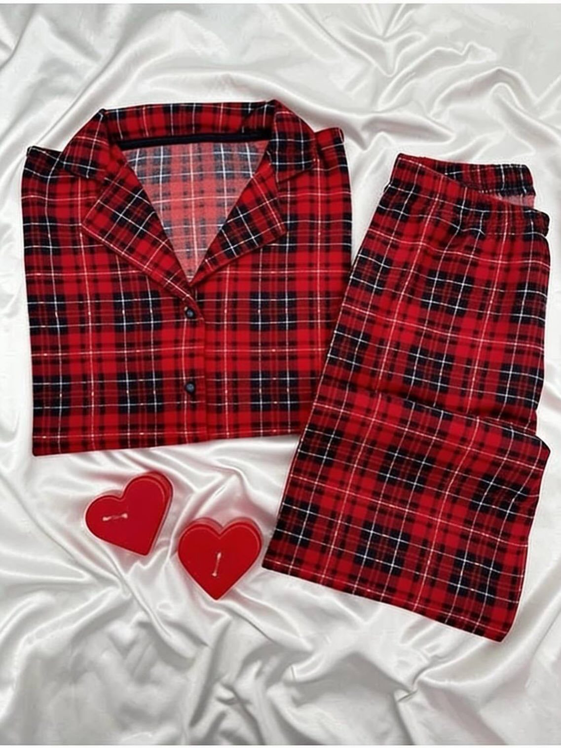 Red and black plaid pajama set with heart candles on white satin fabric.