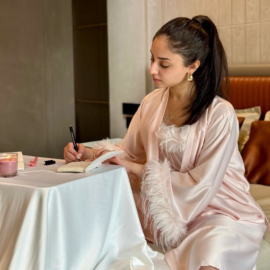 Woman in a pink satin robe with faux-fur trim writing in a notebook.