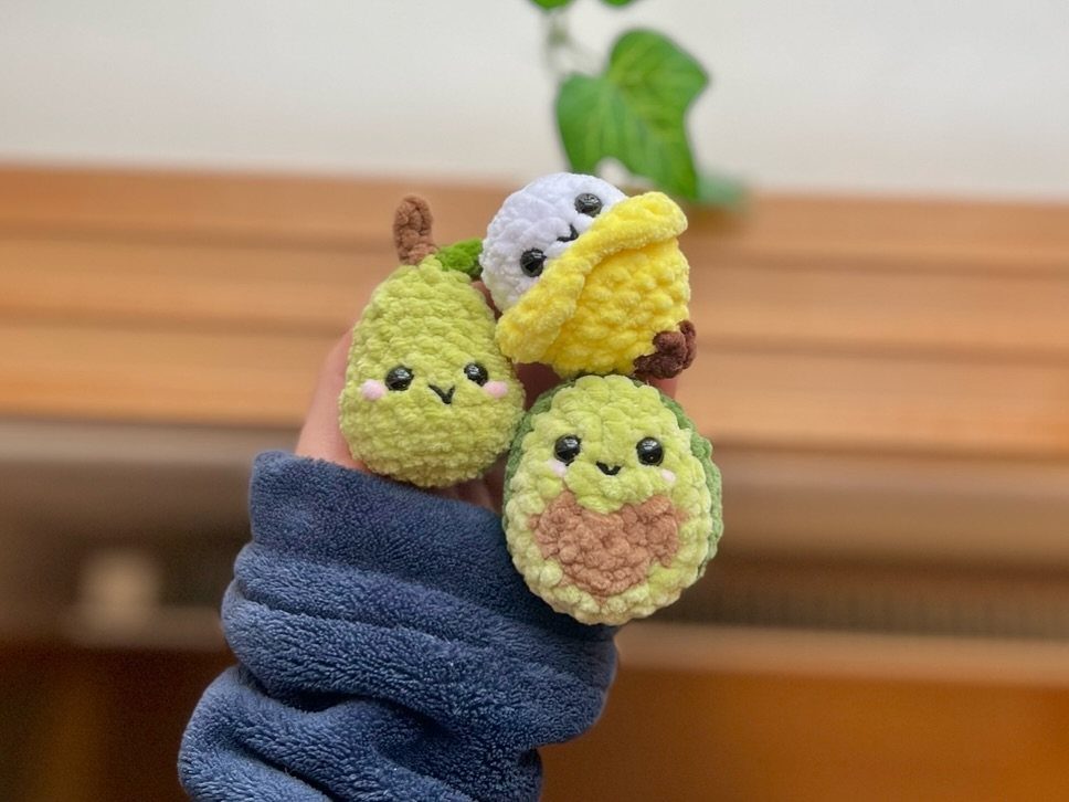 Three small crocheted food plushies held in a hand with a blue sleeve.