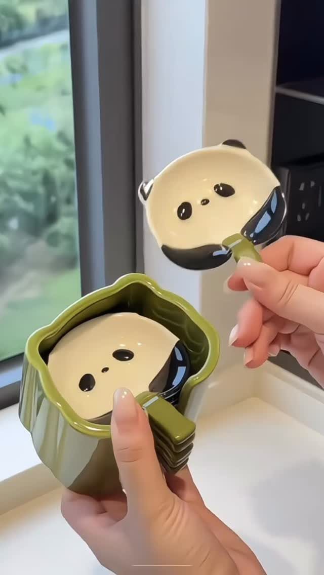 Green ceramic mug and panda-shaped spoon held by hands near a window.