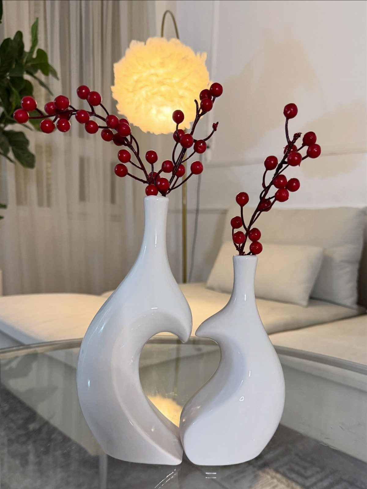 Two white ceramic vases shaped like figures holding red berry branches on glass table