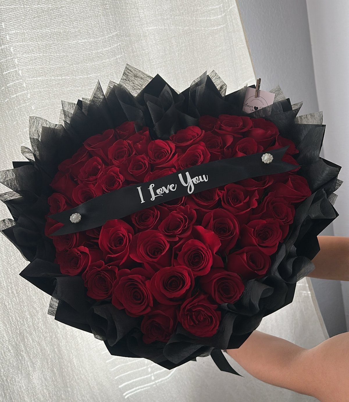 Heart-shaped bouquet of red roses wrapped in black paper with I Love You ribbon