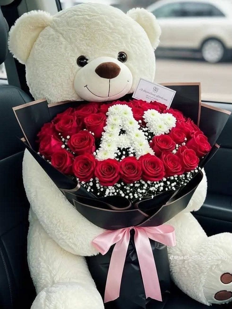 Cream teddy bear holding a red rose bouquet with a white flower heart