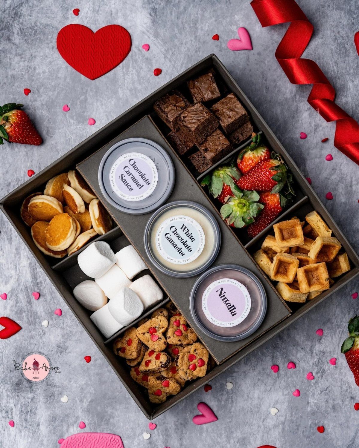 Gourmet dessert platter with brownies, strawberries, waffles, and dipping sauces surrounded by hearts.