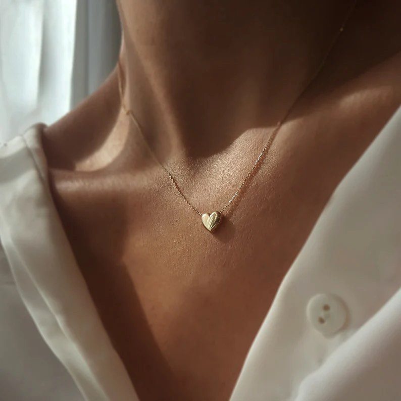 Gold heart pendant necklace worn on a person wearing a white shirt