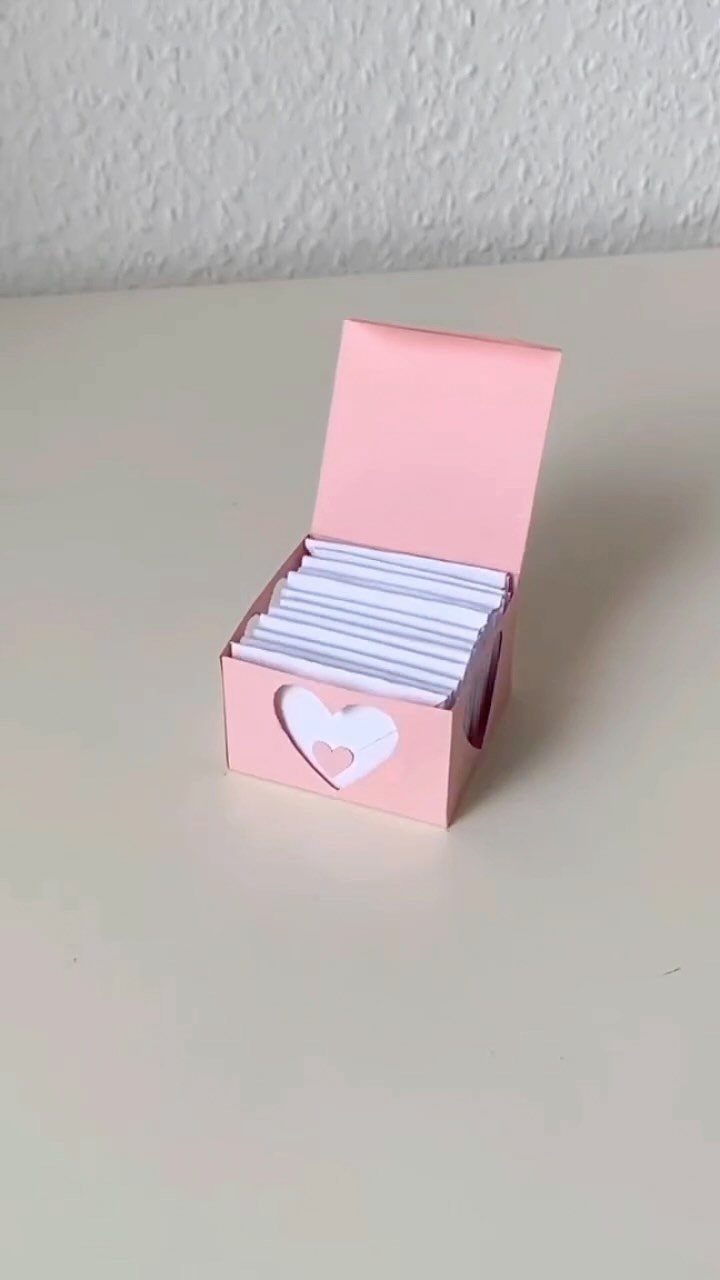 Small pink gift box with heart cutout filled with white paper notes.