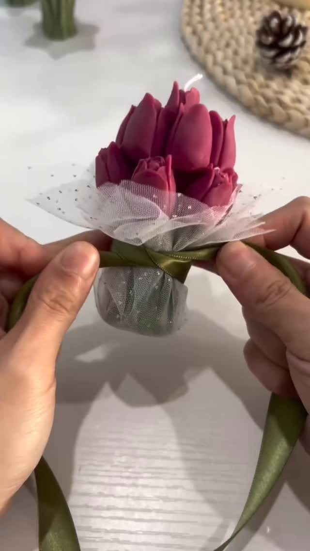 Pink tulip-shaped candle wrapped in white tulle and tied with a green ribbon.
