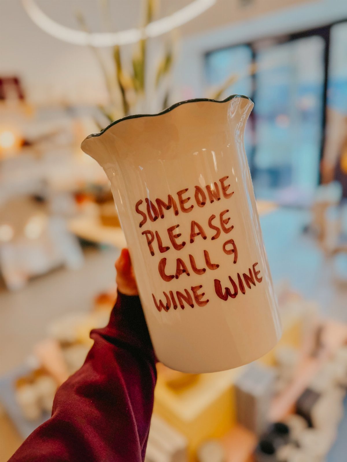 White ceramic pitcher with a wine pun written in red text held by hand.