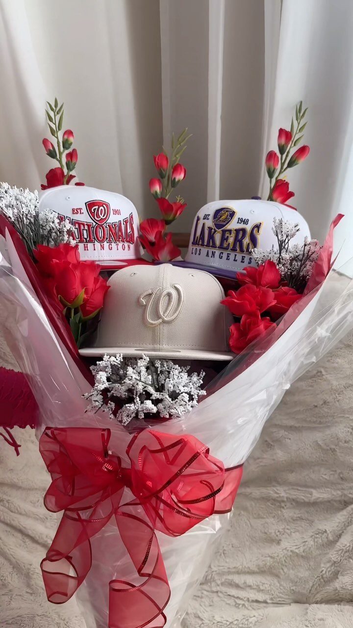 Baseball caps and red roses arranged in a white gift bouquet with red ribbon.