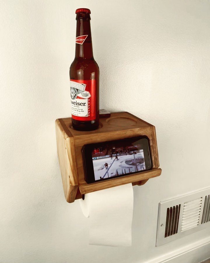 Wooden wall-mounted holder with a smartphone, beer bottle, and toilet paper roll.