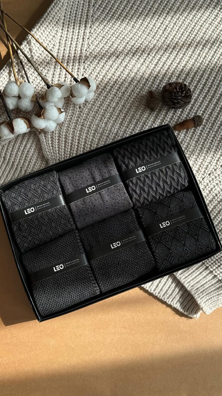 Six pairs of grey and black socks in a black gift box on knit fabric.