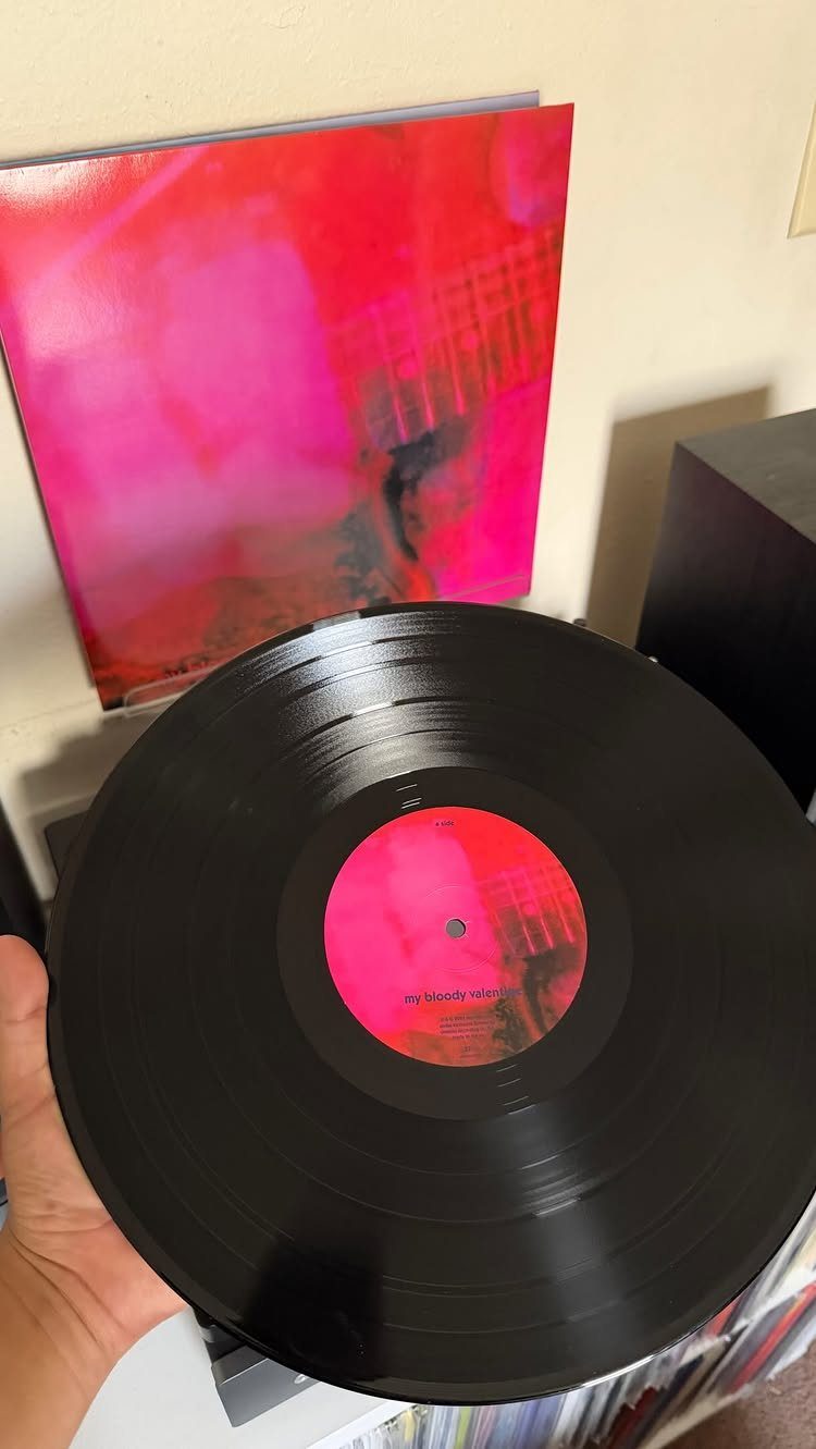 Black vinyl record held in front of a red and pink album cover.