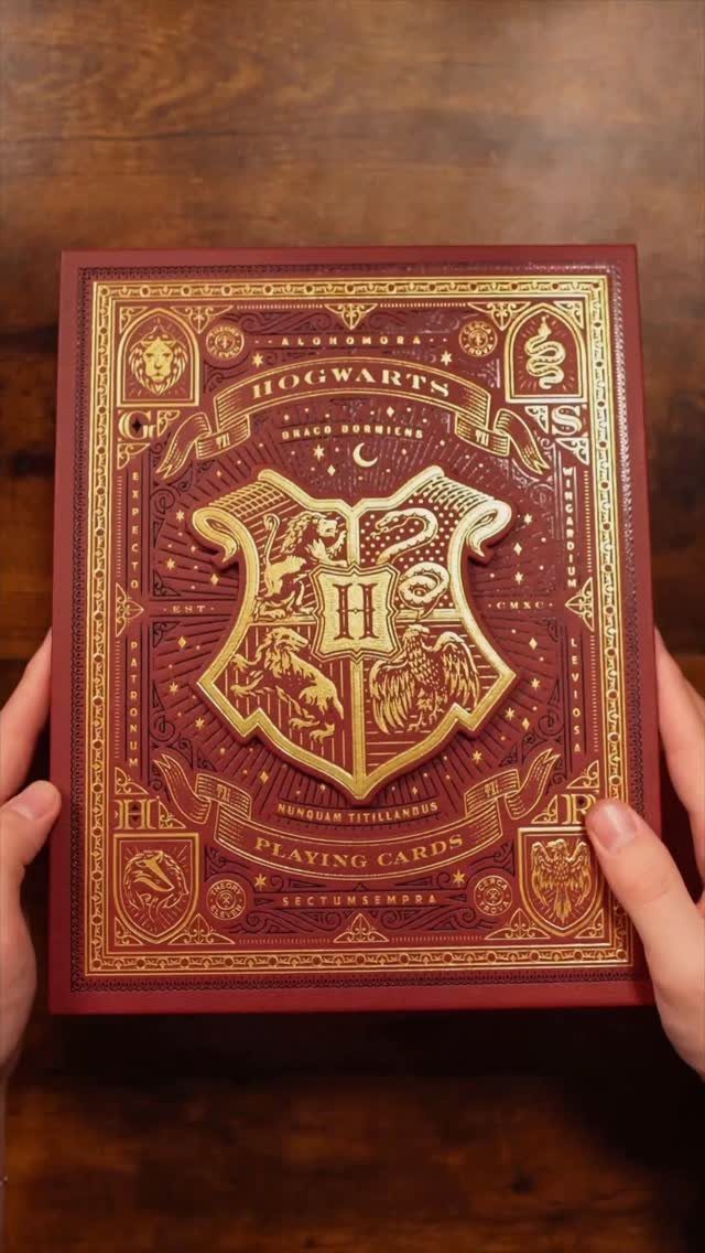 25 Best Harry Potter Gifts for Every Wizarding Fan in 2026 16 Red Hogwarts playing cards box with gold embossed crest held by two hands.
