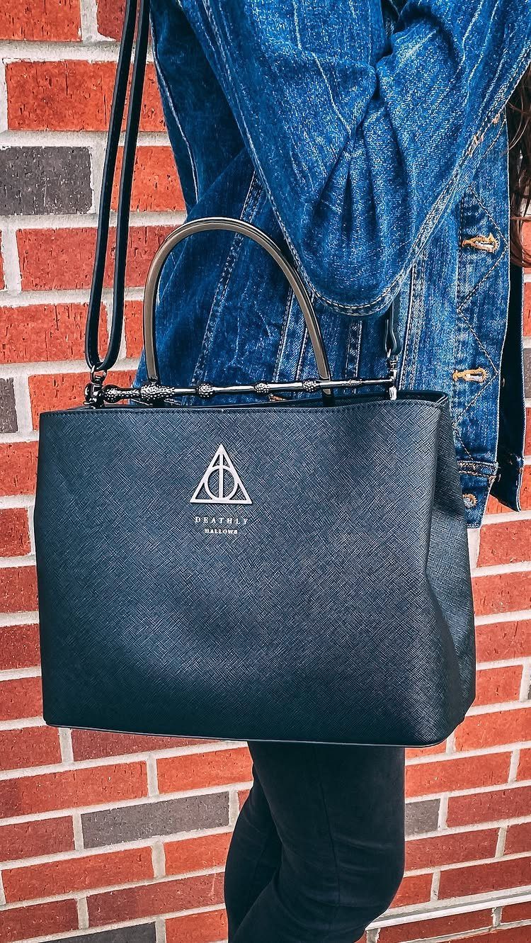 25 Best Harry Potter Gifts for Every Wizarding Fan in 2026 19 Black textured handbag with white Deathly Hallows symbol held against a brick wall.
