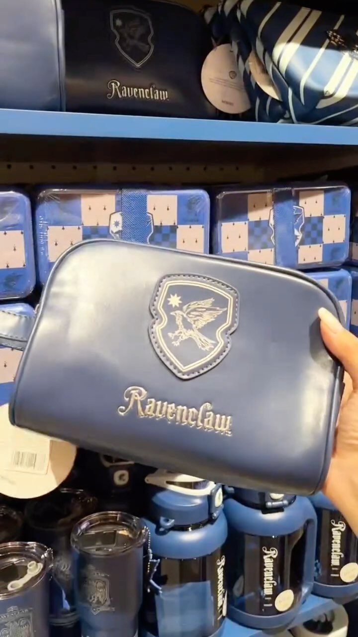 25 Best Harry Potter Gifts for Every Wizarding Fan in 2026 9 Blue Ravenclaw cosmetic bag held in front of shelves of themed merchandise.
