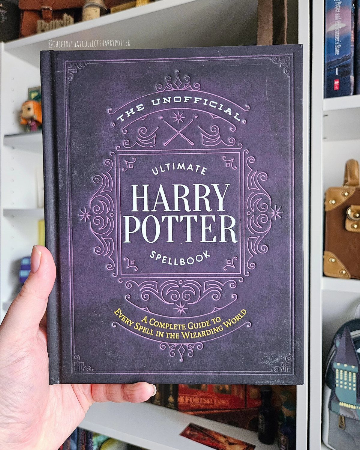 25 Best Harry Potter Gifts for Every Wizarding Fan in 2026 12 Purple hardcover Harry Potter spellbook held by a hand in front of a bookshelf