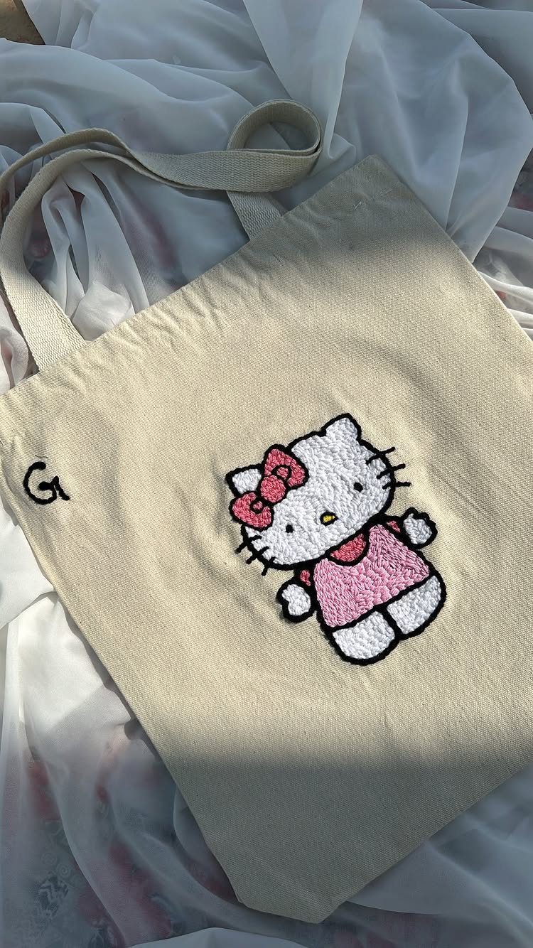 Beige canvas tote bag with an embroidered Hello Kitty wearing a pink dress.