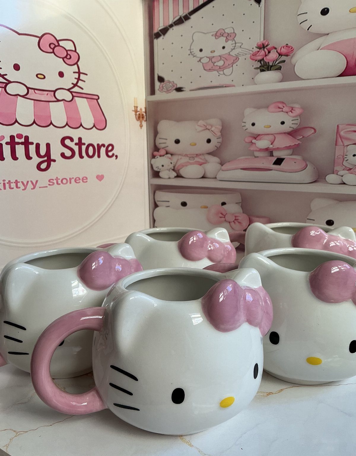 White Hello Kitty ceramic mugs with pink bows on a marble surface.