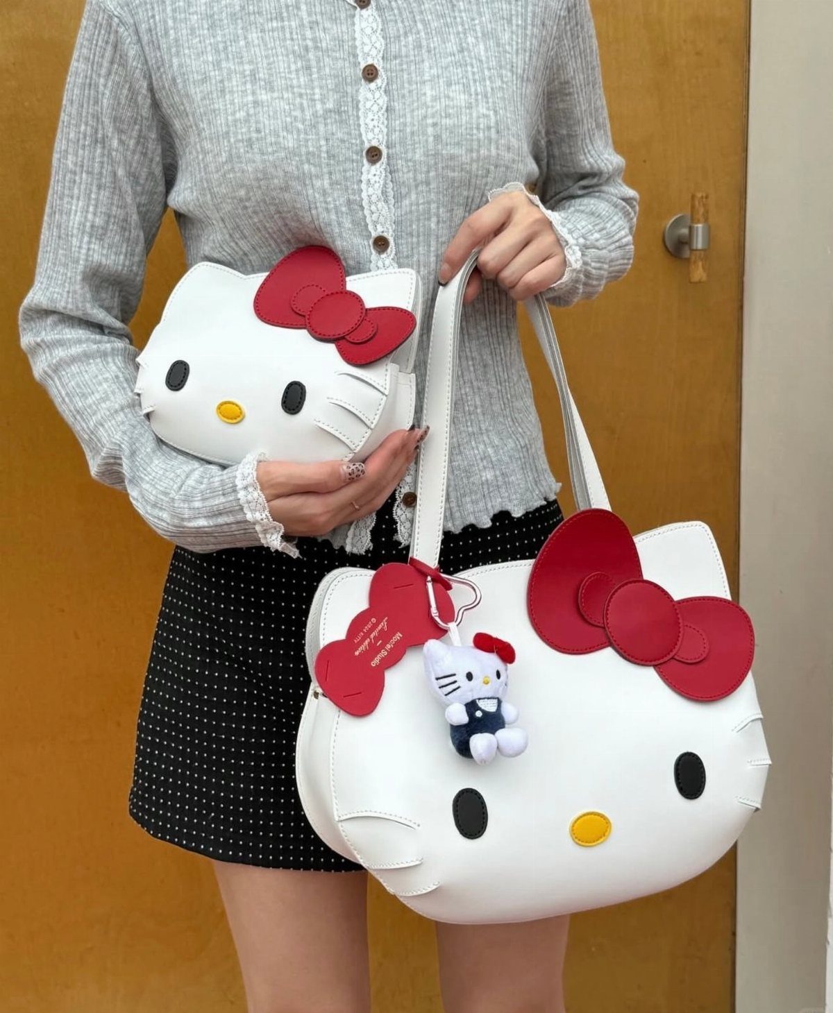 Two white Hello Kitty shaped bags held by a person in a grey cardigan.