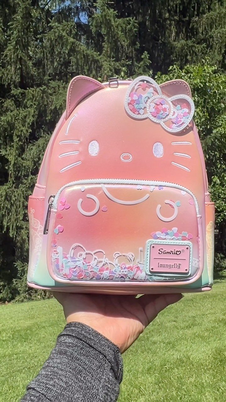 Iridescent Hello Kitty backpack with pink gradient held against a green outdoor background