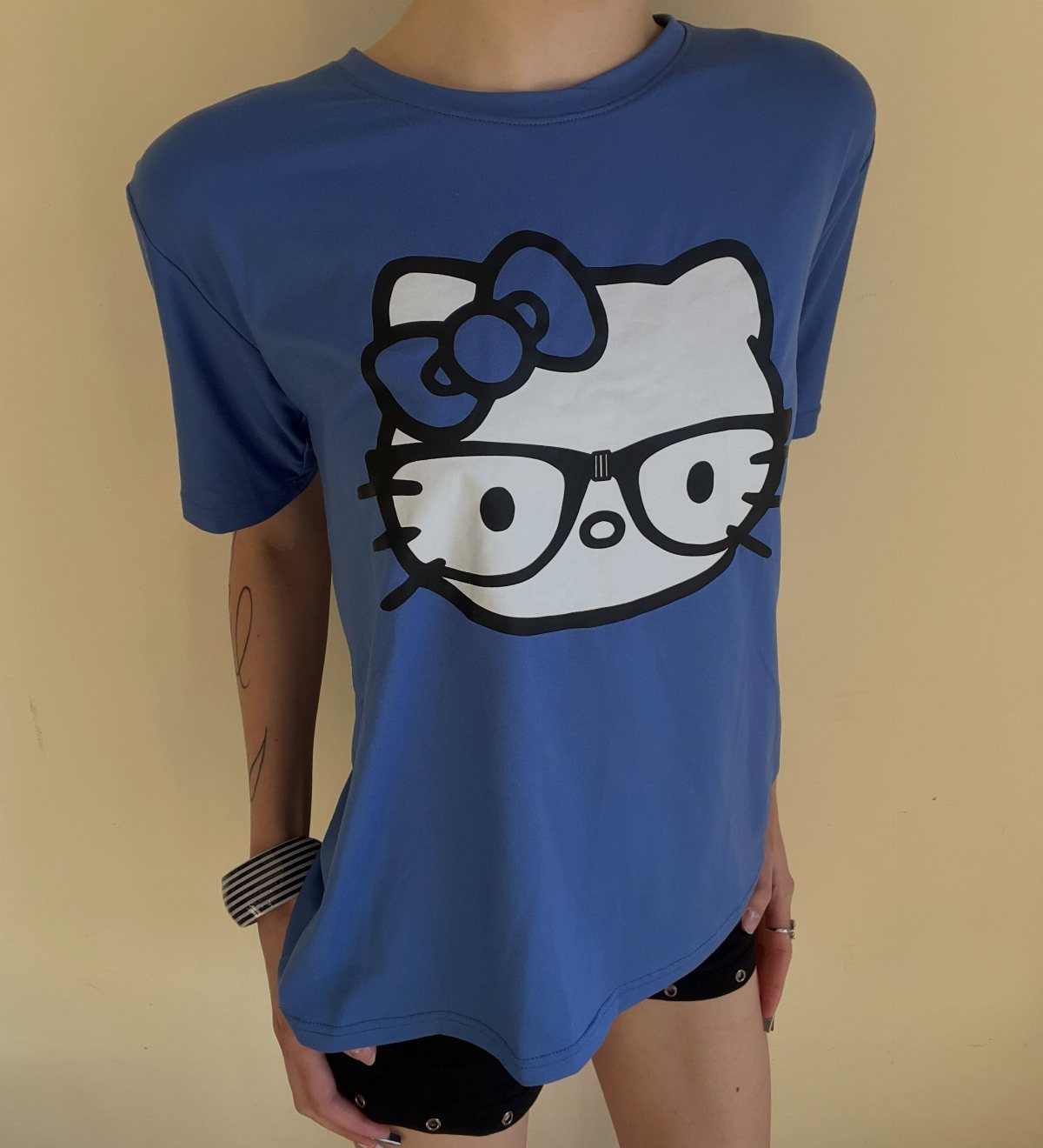 Blue t-shirt featuring Hello Kitty wearing black nerd glasses worn by a person.
