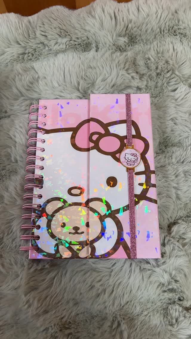 Hello Kitty spiral notebook with a pink elastic band on grey faux fur