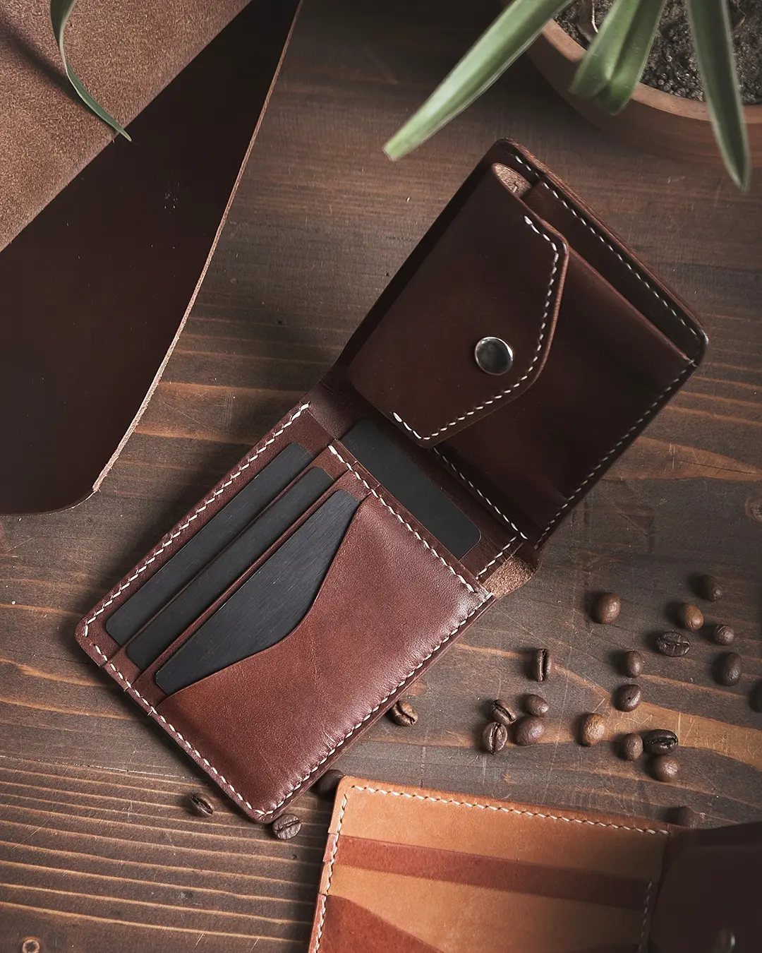 Brown leather bifold wallet open on a wooden table with coffee beans.