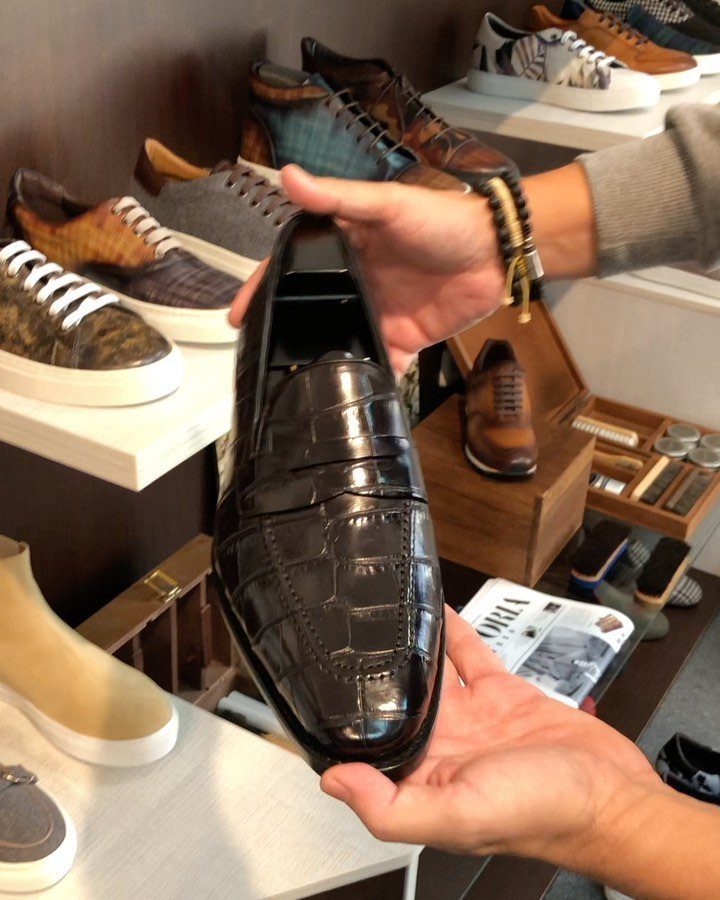 Black crocodile-skin loafer held by hands in a luxury men's shoe store