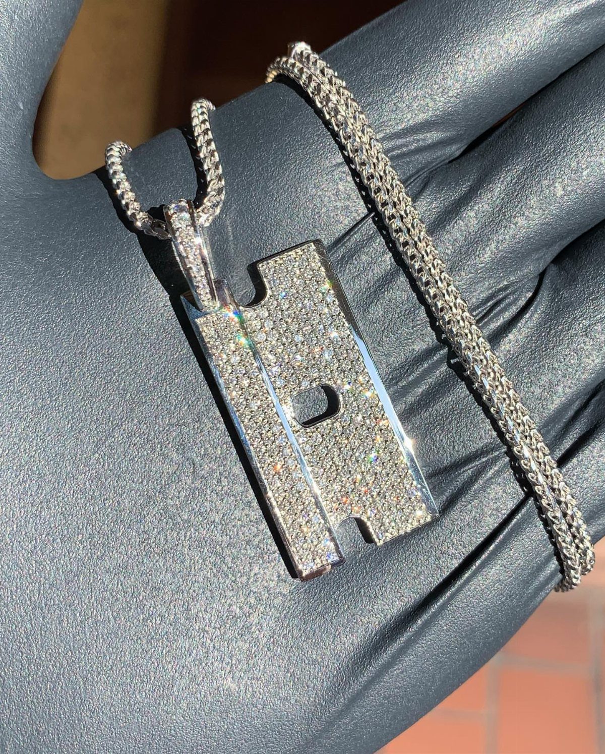 Silver diamond-encrusted pendant necklace held by a hand in a grey glove.