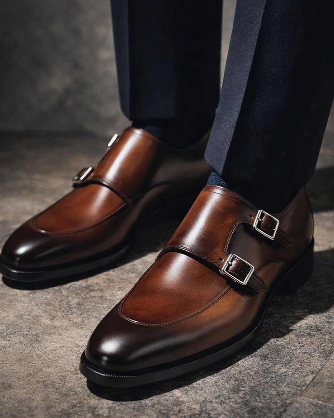 Brown leather double-monk strap shoes worn with dark navy dress trousers.