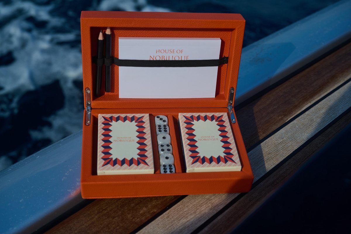 Orange leather travel case with playing cards and dominoes on a boat deck