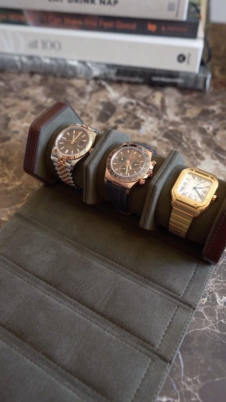 Three luxury gold and silver wristwatches displayed on a green suede watch roll.