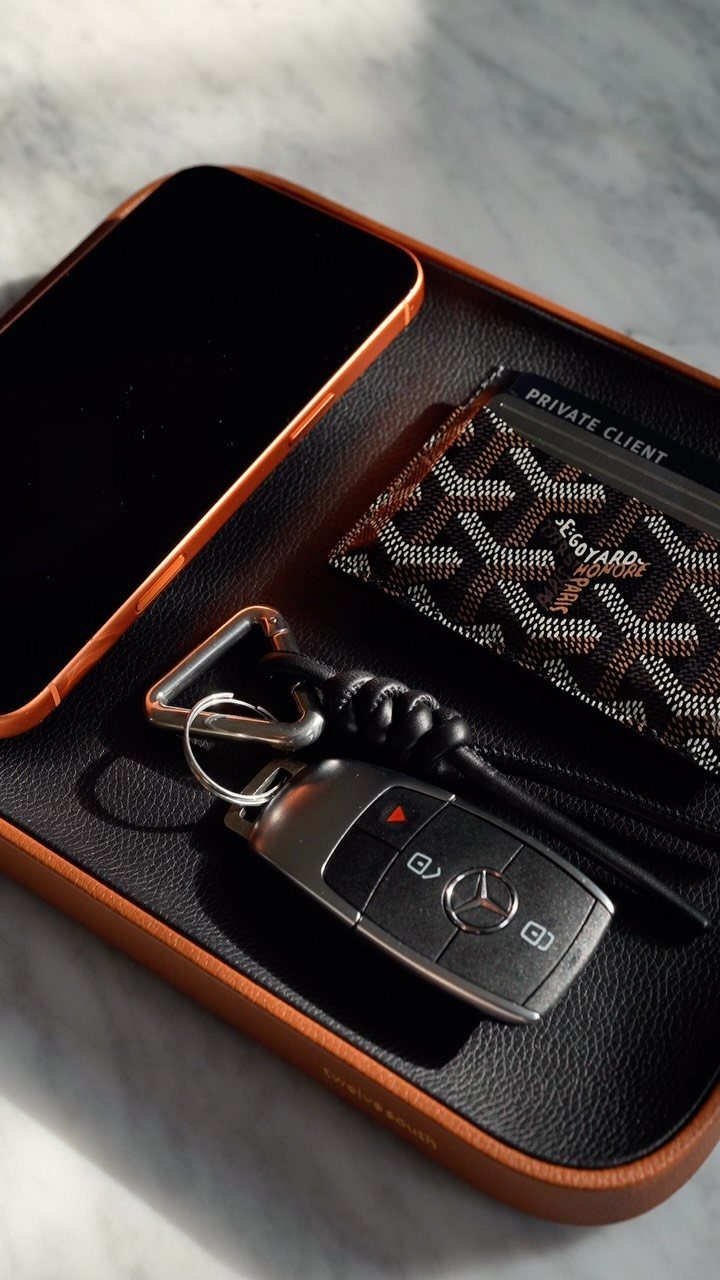Brown leather charging tray holding a smartphone, patterned wallet, and Mercedes car key.