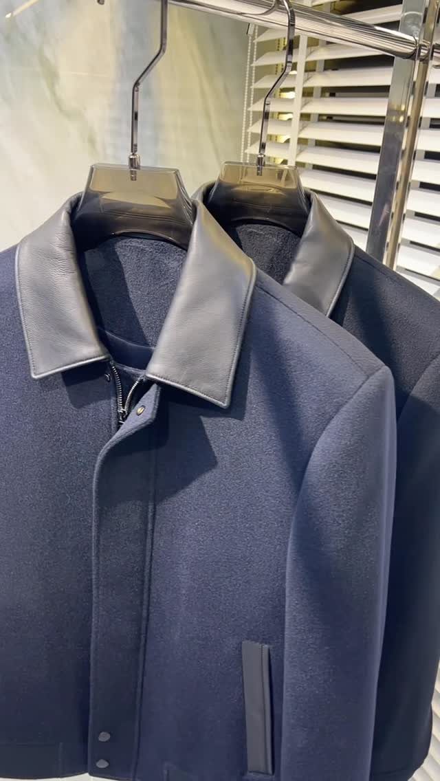 Navy blue wool jackets with black leather collars hanging on a silver rack.