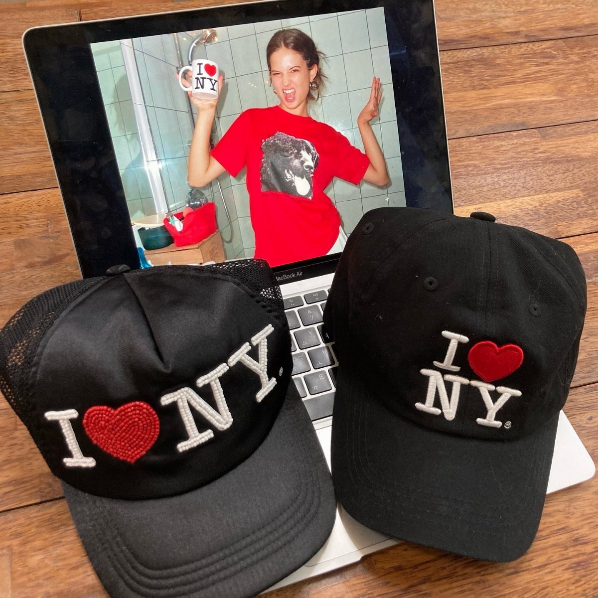 Two black I Love NY baseball caps resting on a white laptop keyboard.