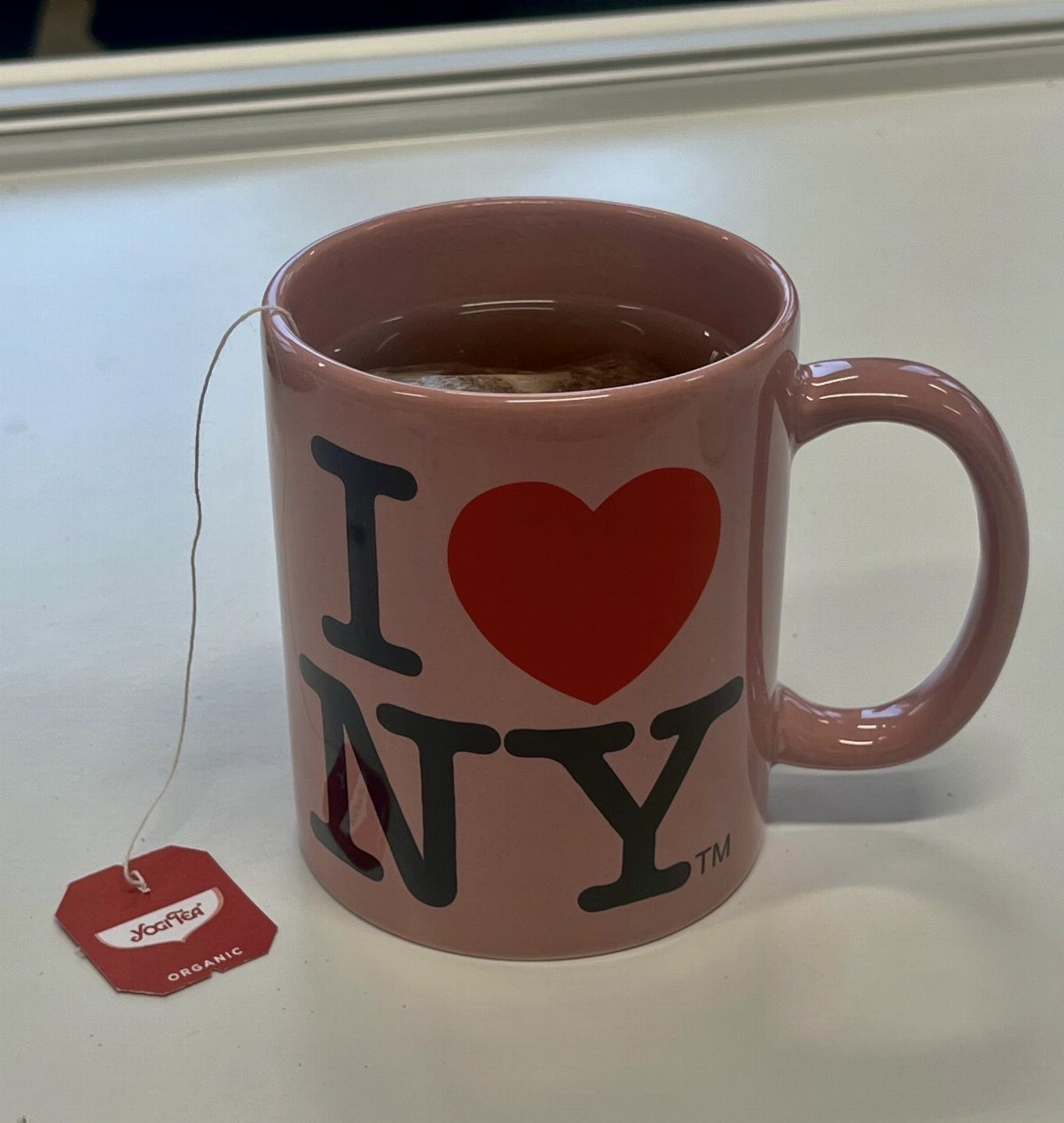 Pink I Love NY mug filled with tea on a white surface.