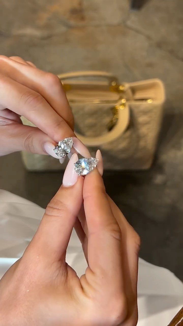 Luxury Gifts for Women: 11 Ideas from Candles to Jewelry 9 Diamond earrings held by manicured hands with a luxury handbag in the background